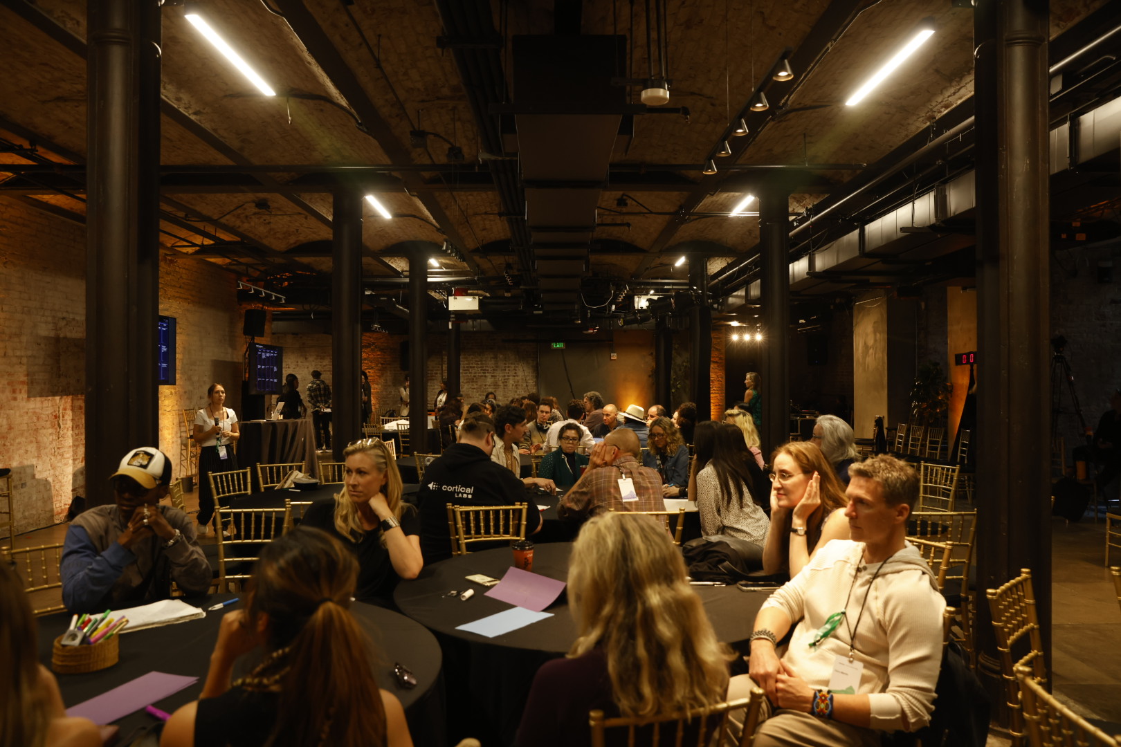 A working session at Human+Tech Week: people at round tables with papers and laptops